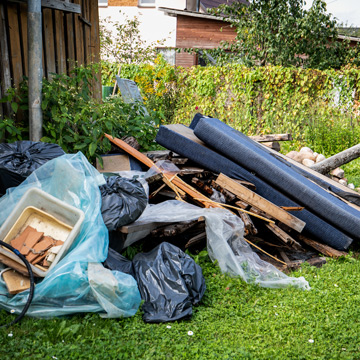 a cluttered pile of debris including black garbage bags wood planks and an old container scattered in a grassy area