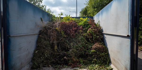 a filled garden waste container with various plants and leaves for disposal and composting environmental sustainability